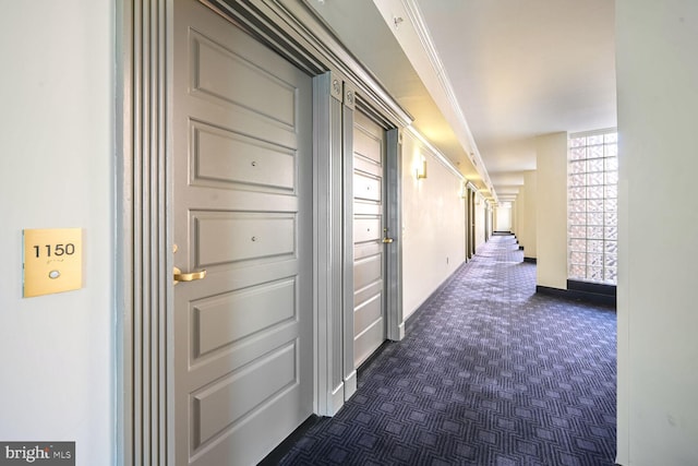 hall with dark colored carpet and ornamental molding