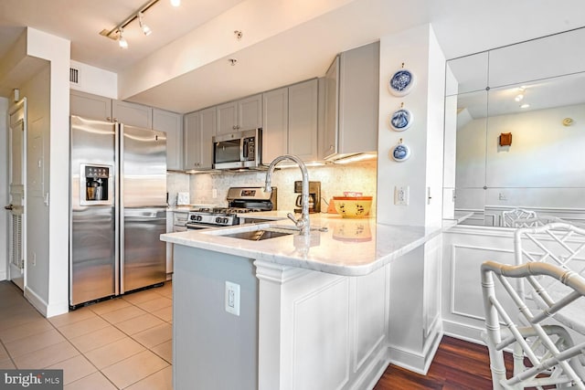 kitchen with appliances with stainless steel finishes, sink, gray cabinetry, light tile patterned floors, and kitchen peninsula