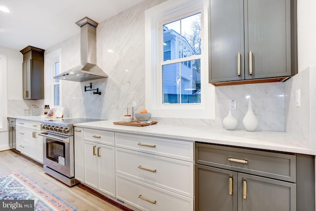 kitchen with gray cabinetry, island range hood, decorative backsplash, stainless steel range with electric cooktop, and light wood-type flooring