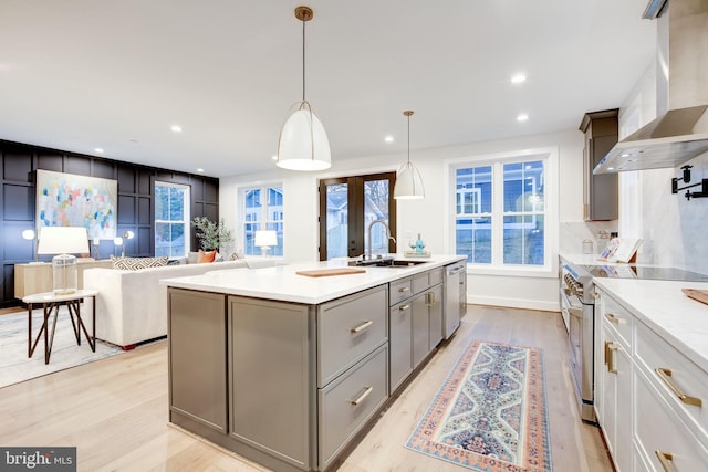 kitchen featuring decorative light fixtures, sink, a kitchen island with sink, stainless steel appliances, and wall chimney range hood