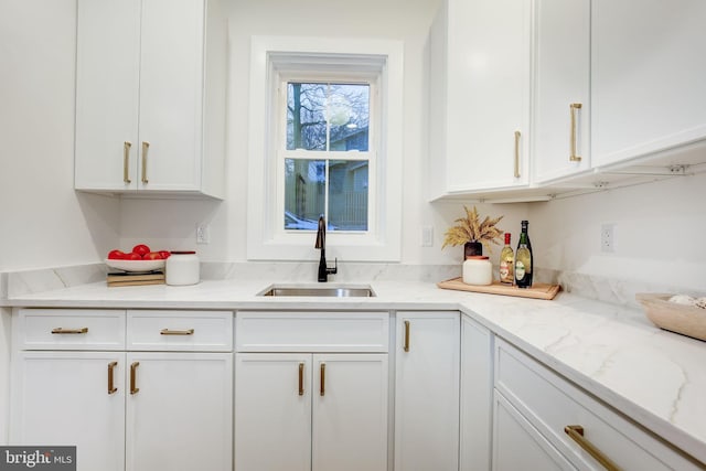 kitchen with light stone counters, sink, and white cabinets