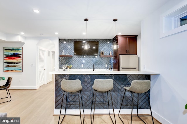 kitchen featuring stainless steel fridge, a kitchen breakfast bar, light hardwood / wood-style floors, decorative light fixtures, and kitchen peninsula