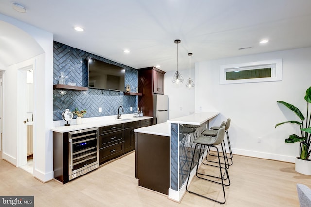 bar with pendant lighting, refrigerator, backsplash, wine cooler, and light hardwood / wood-style flooring