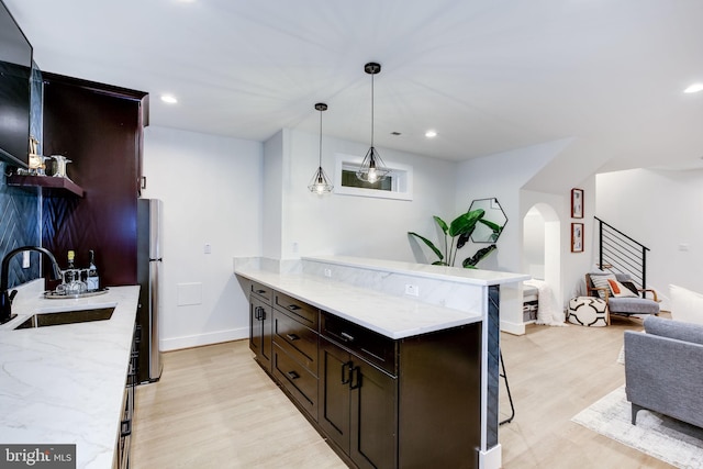 kitchen featuring sink, a breakfast bar area, stainless steel fridge, decorative light fixtures, and light wood-type flooring