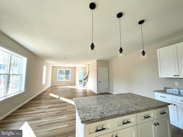 kitchen with light stone counters, light hardwood / wood-style flooring, white cabinets, and decorative light fixtures