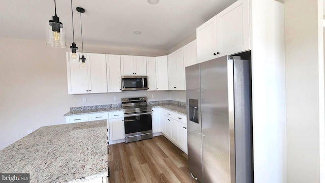 kitchen featuring light stone countertops, stainless steel appliances, pendant lighting, light hardwood / wood-style floors, and white cabinetry