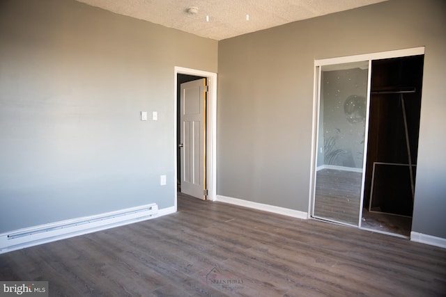 unfurnished bedroom with a closet, a textured ceiling, a baseboard heating unit, and dark wood-type flooring