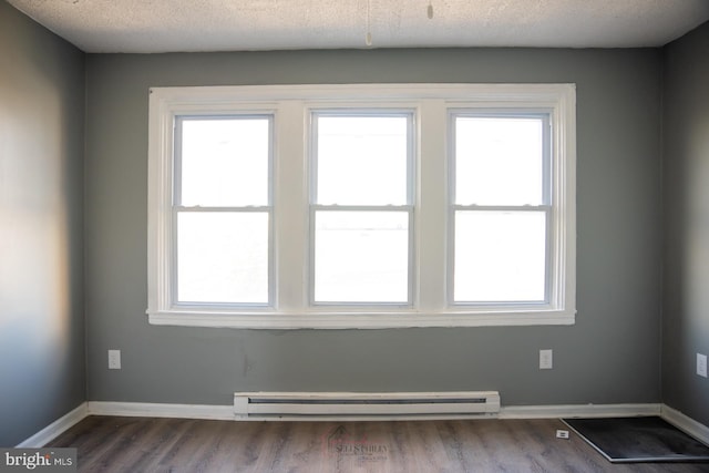 empty room with hardwood / wood-style floors, a textured ceiling, plenty of natural light, and a baseboard heating unit