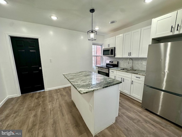 kitchen featuring pendant lighting, appliances with stainless steel finishes, a center island, light stone counters, and white cabinets