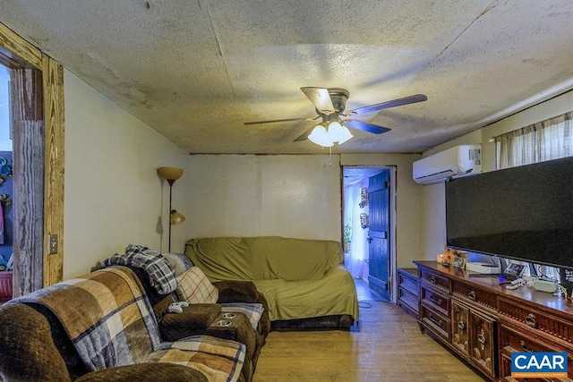 living room with a wall mounted AC, ceiling fan, light hardwood / wood-style flooring, and a textured ceiling