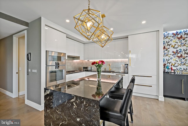 kitchen with appliances with stainless steel finishes, white cabinets, light hardwood / wood-style floors, a kitchen island, and a breakfast bar area