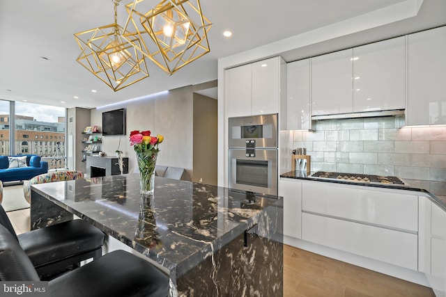 kitchen featuring exhaust hood, tasteful backsplash, decorative light fixtures, white cabinetry, and stainless steel appliances