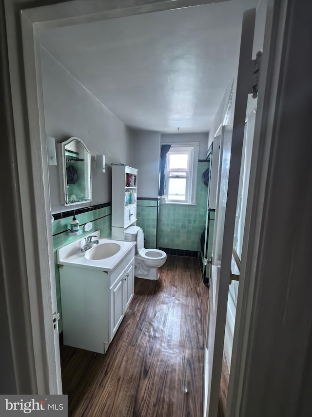 bathroom with a shower, wood-type flooring, toilet, vanity, and tile walls