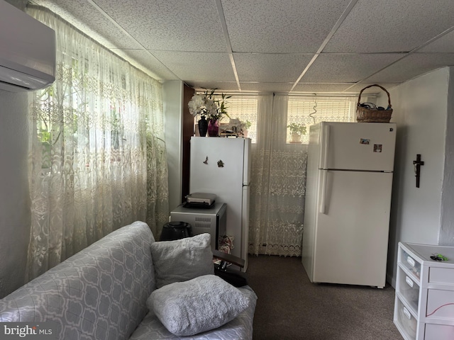 interior space with carpet flooring, white refrigerator, an AC wall unit, and a paneled ceiling