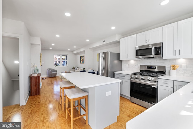 kitchen with white cabinetry, a center island, a kitchen breakfast bar, light hardwood / wood-style flooring, and appliances with stainless steel finishes