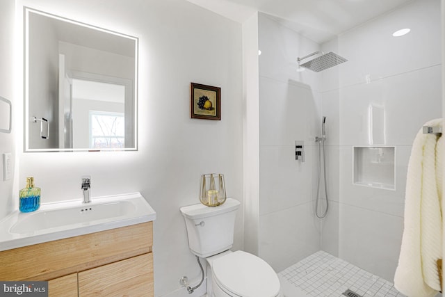 bathroom featuring a tile shower, vanity, and toilet