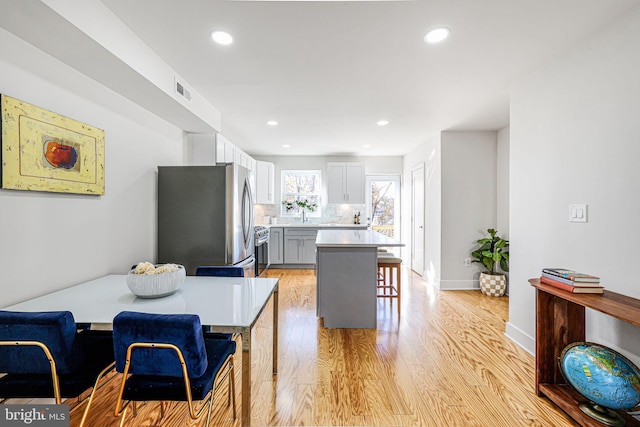 kitchen featuring gray cabinetry, stainless steel appliances, tasteful backsplash, a kitchen bar, and light wood-type flooring