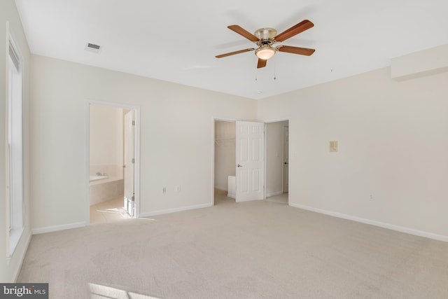 unfurnished bedroom featuring connected bathroom, a spacious closet, light colored carpet, ceiling fan, and a closet