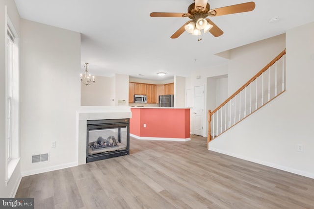 unfurnished living room featuring ceiling fan with notable chandelier, a multi sided fireplace, and light hardwood / wood-style floors