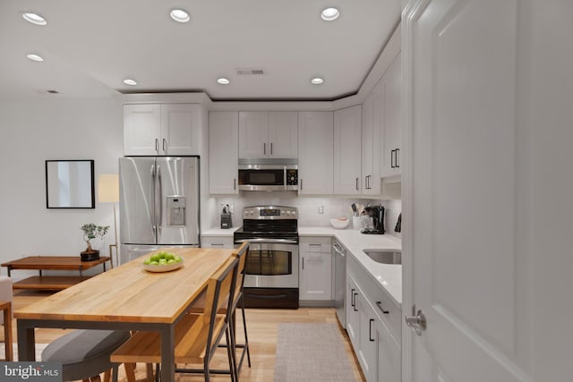 kitchen with white cabinets, tasteful backsplash, appliances with stainless steel finishes, and light hardwood / wood-style flooring