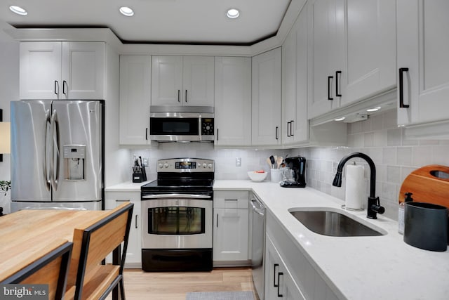 kitchen with sink, tasteful backsplash, light stone counters, light hardwood / wood-style flooring, and appliances with stainless steel finishes