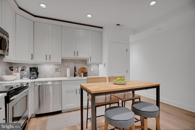 kitchen featuring backsplash, white cabinets, sink, light hardwood / wood-style flooring, and stainless steel appliances