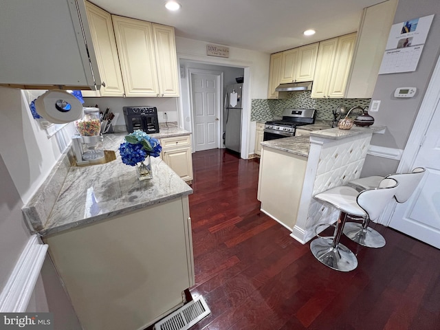 kitchen with dark hardwood / wood-style floors, light stone countertops, stainless steel appliances, and a breakfast bar area