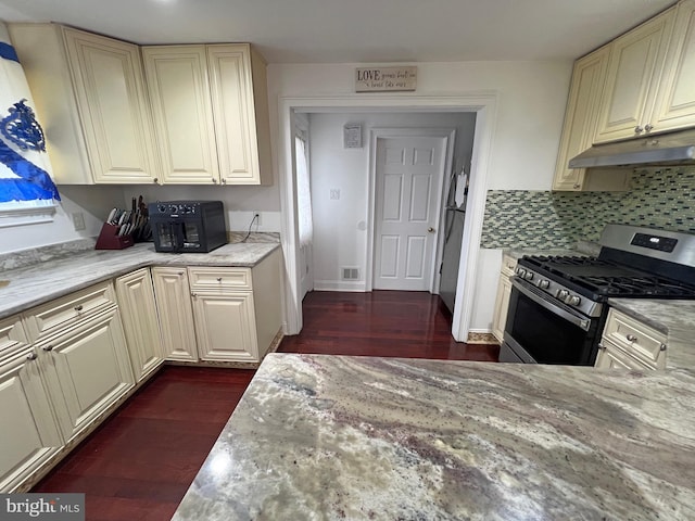 kitchen with light stone countertops, backsplash, and stainless steel range with gas cooktop