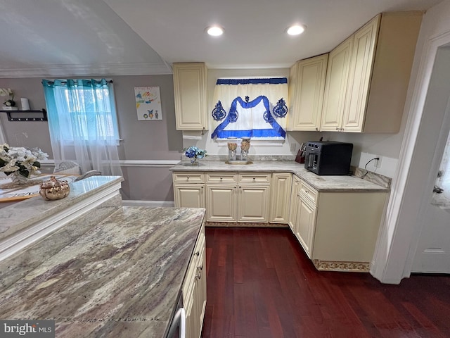 kitchen with light stone countertops, ornamental molding, dark wood-type flooring, and cream cabinets