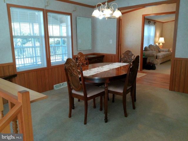 carpeted dining space featuring wooden walls, ornamental molding, and an inviting chandelier