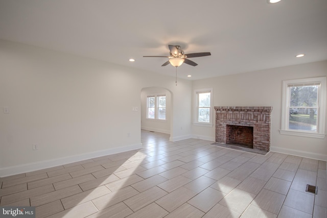 unfurnished living room featuring ceiling fan and a brick fireplace