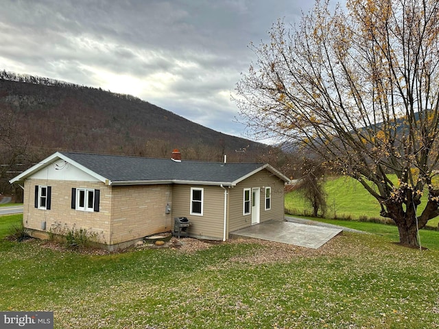 back of house with a mountain view, a patio area, and a yard