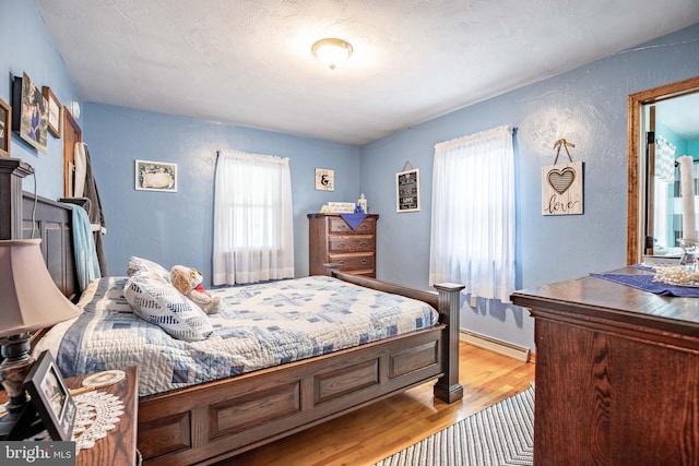 bedroom with a textured ceiling, a baseboard radiator, and light hardwood / wood-style flooring