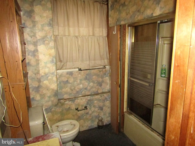 bathroom with toilet and bath / shower combo with glass door