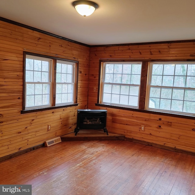 unfurnished room featuring wood-type flooring, a wood stove, and wooden walls