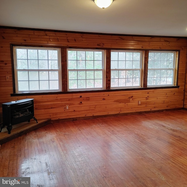 unfurnished room featuring hardwood / wood-style floors, wood walls, and a wood stove