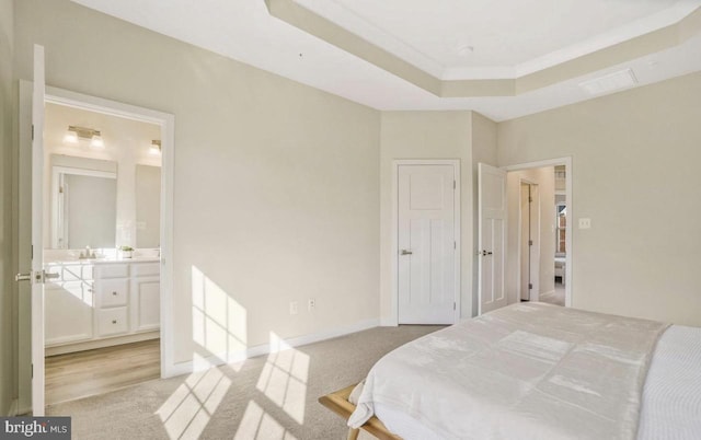 carpeted bedroom with a raised ceiling, ensuite bath, and sink