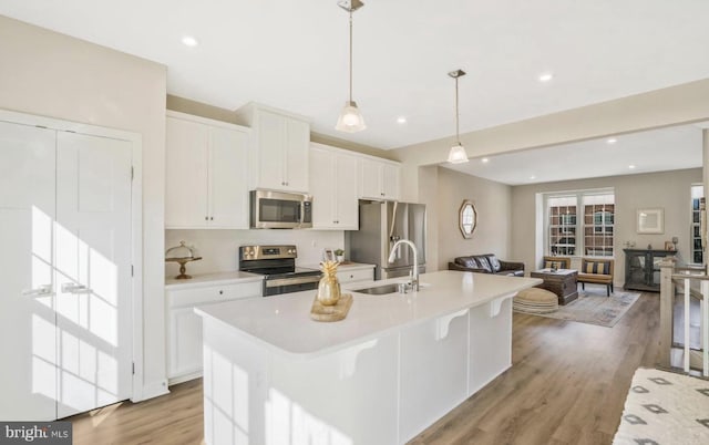 kitchen with a center island with sink, sink, appliances with stainless steel finishes, decorative light fixtures, and white cabinetry