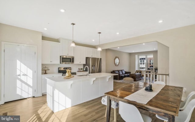 kitchen featuring appliances with stainless steel finishes, a kitchen island with sink, decorative light fixtures, light hardwood / wood-style flooring, and white cabinetry