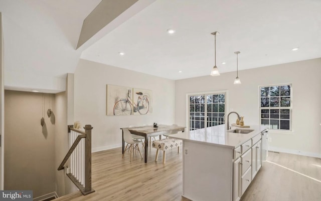 kitchen with a kitchen island with sink, sink, hanging light fixtures, and light hardwood / wood-style floors