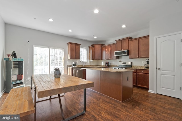 kitchen featuring a center island, sink, stainless steel appliances, light stone counters, and dark hardwood / wood-style flooring