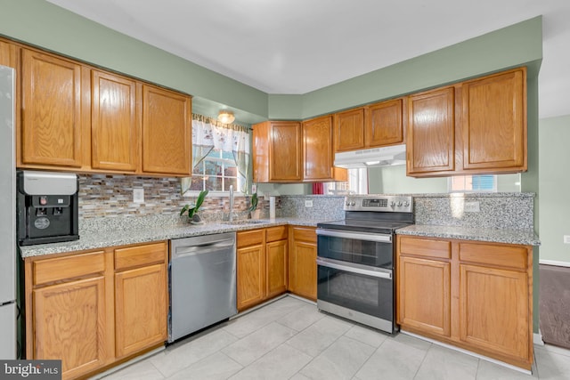 kitchen with light stone countertops, sink, backsplash, light tile patterned flooring, and appliances with stainless steel finishes