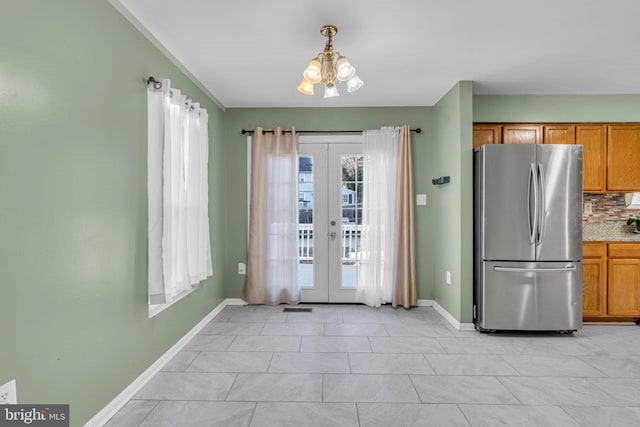 kitchen featuring stainless steel refrigerator, french doors, pendant lighting, a chandelier, and decorative backsplash