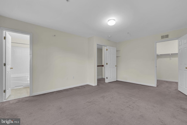 unfurnished bedroom featuring carpet, a closet, ensuite bath, and a spacious closet