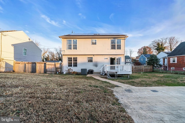 rear view of property with a lawn, solar panels, central air condition unit, and a wooden deck