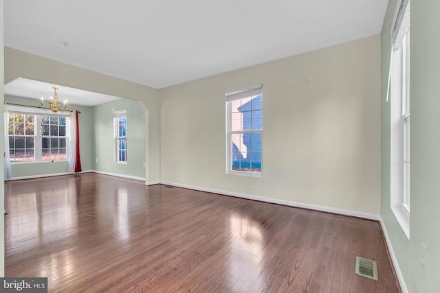 empty room featuring hardwood / wood-style floors, a healthy amount of sunlight, and an inviting chandelier