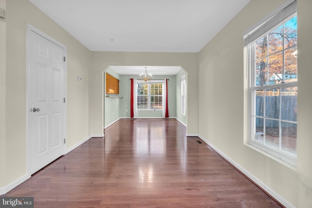 empty room featuring a chandelier, dark wood-type flooring, and a healthy amount of sunlight