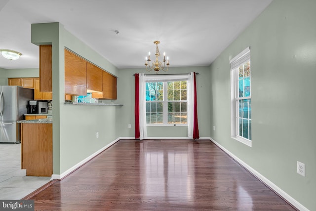 unfurnished dining area featuring light wood-type flooring, an inviting chandelier, and a wealth of natural light