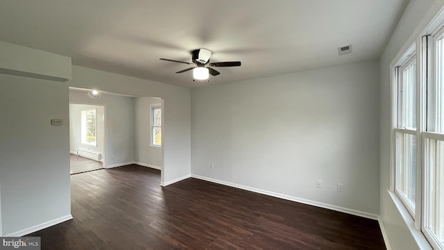 spare room with baseboard heating, ceiling fan, and dark wood-type flooring