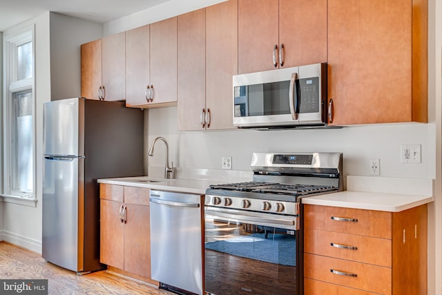 kitchen with stainless steel appliances, light countertops, a sink, and light wood-style flooring